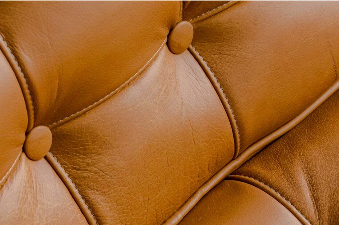 Close-up of brown leather upholstery with button-tufted stitching, showing texture, seams, and natural creases in the material.
